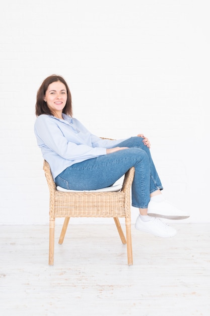 Pretty plus size model woman in shirt and jeans posing in studio on chair, white background with copy space.