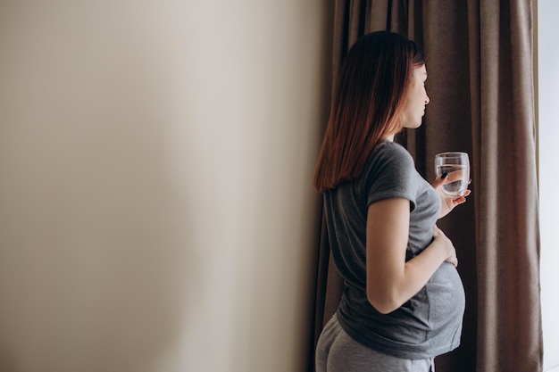 Красивая беременная женщина пьет воду, лежа дома на диване
