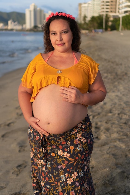 Pretty pregnant woman gently touching her belly while standing on the beach