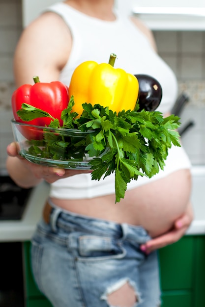 pretty pregnant woman holding a plate with vegetables and herbs