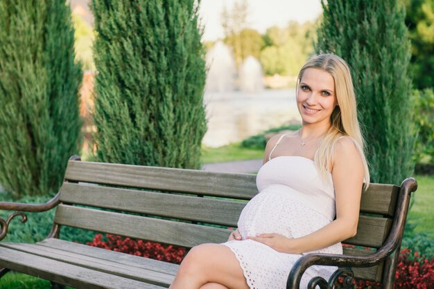 Pretty pregnant woman sitting on the bench outdoor looking into the camera