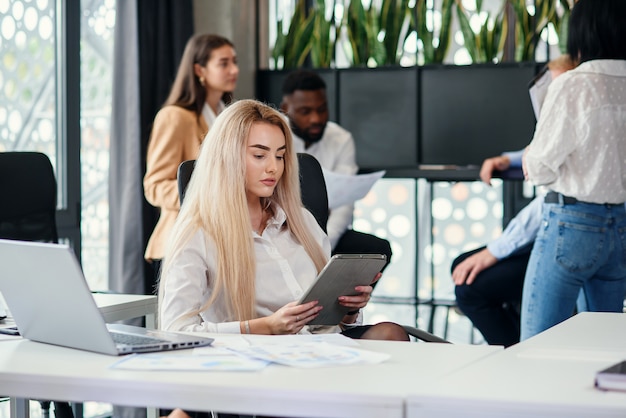 Dati entranti del giovane responsabile femminile abbastanza intenzionale dell'ufficio dal rapporto finanziario al computer portatile nell'ufficio moderno