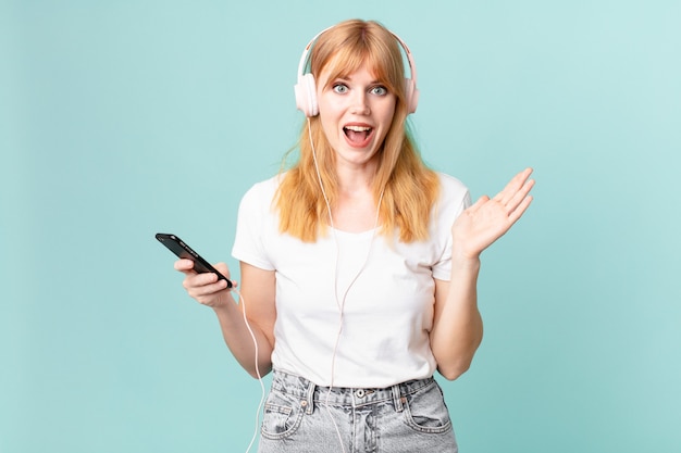 pretty red head woman feeling happy and astonished at something unbelievable and listening music with headphones