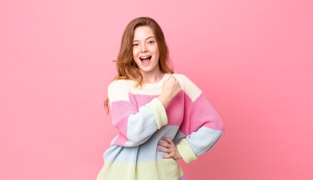 Pretty red head woman feeling happy and facing a challenge or celebrating