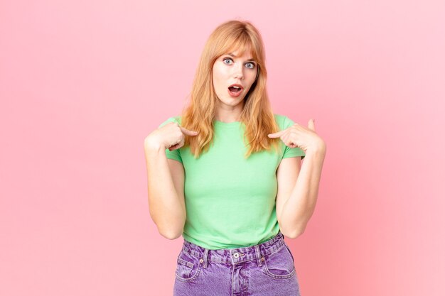 Pretty red head woman feeling happy and pointing to self with an excited