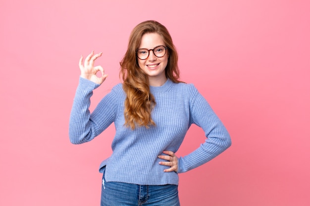 Pretty red head woman feeling happy, showing approval with okay gesture