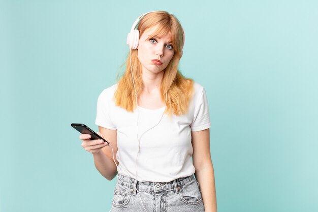 Una bella donna dai capelli rossi che si sente triste e piagnucolona con uno sguardo infelice e piange e ascolta musica con le cuffie