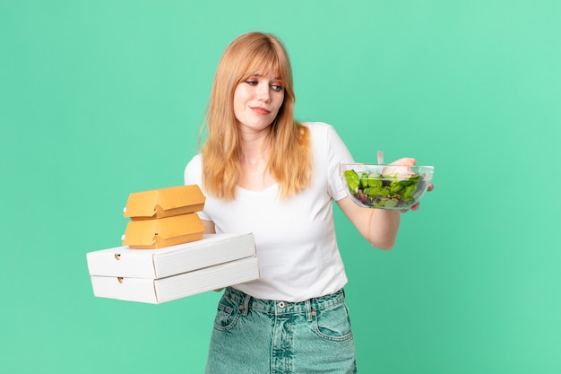 Pretty red head woman holding fast food boxes and a salad