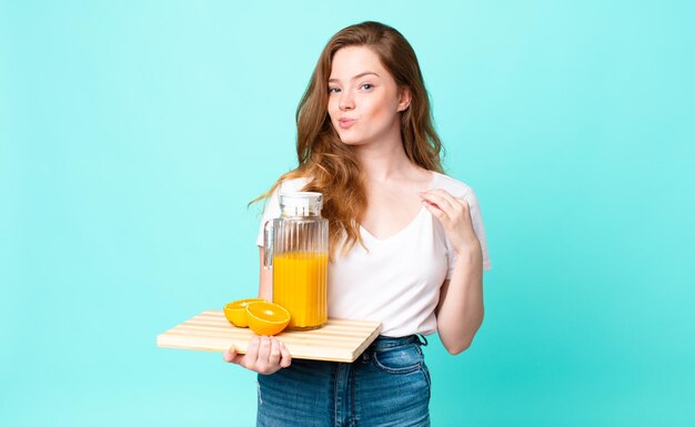 Pretty red head woman looking arrogant, successful, positive and proud and holding an orange juice