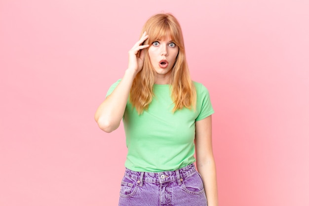 Pretty red head woman looking surprised, realizing a new thought, idea or concept