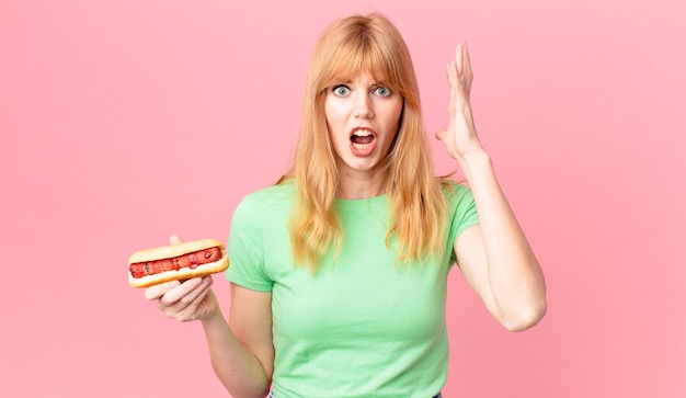 pretty red head woman screaming with hands up in the air and holding a hot dog