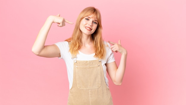 自分の広い笑顔を自信を持って指差して笑っているかなり赤い頭の女性