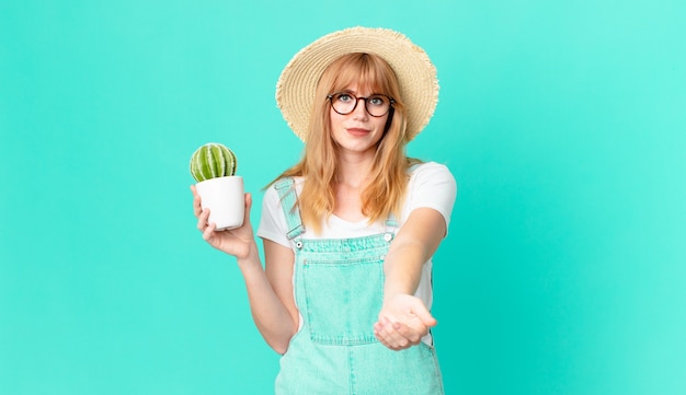 Pretty red head woman smiling happily with friendly and  offering and showing a concept and holding a potted cactus. farmer concept