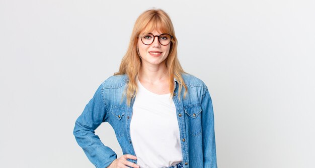 Pretty red head woman smiling happily with a hand on hip and confident