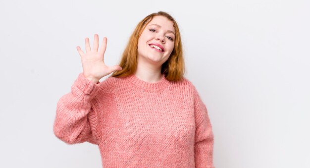 Pretty red head woman smiling and looking friendly showing number five or fifth with hand forward counting down