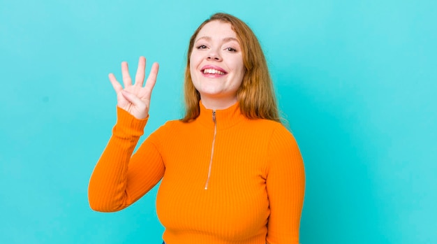 Pretty red head woman smiling and looking friendly showing number four or fourth with hand forward counting down