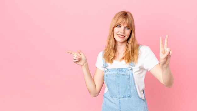 Pretty red head woman smiling and looking friendly, showing number two