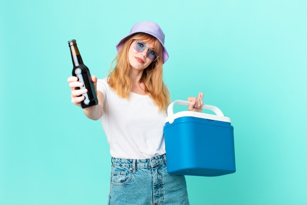 Pretty red head woman with a portable refrigerator and a beer