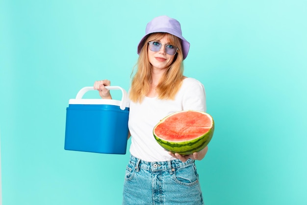Pretty red head woman with a portable refrigerator and a watermelon
