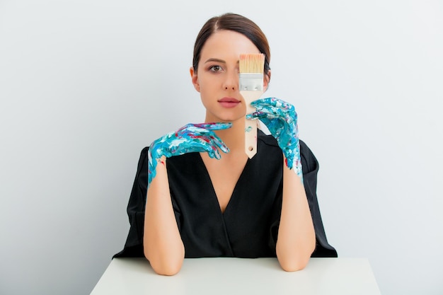 Pretty redhead caucasian woman in black dress and painted hands with brush sitting at white table in lagom style on white background