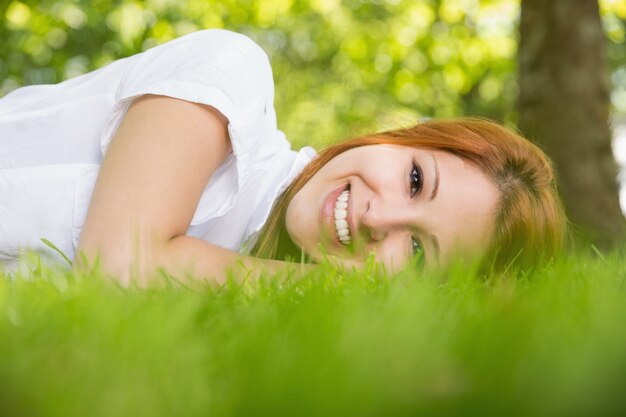 Pretty redhead smiling at camera lying on the grass