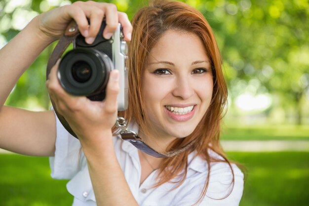 Pretty redhead taking a photo in the park