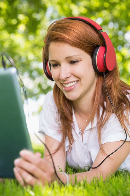 Pretty redhead using her tablet pc while listening to music in the park 