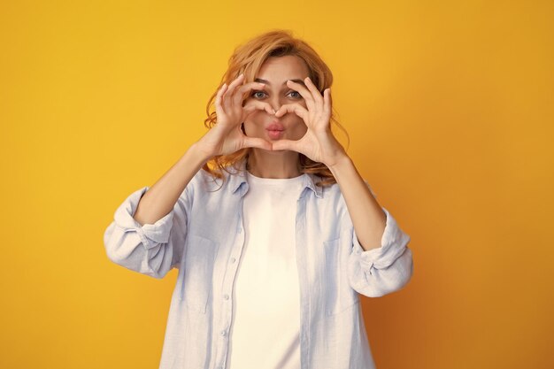 Pretty romantic young woman making a heart gesture showing love\
and affection grateful gesture with