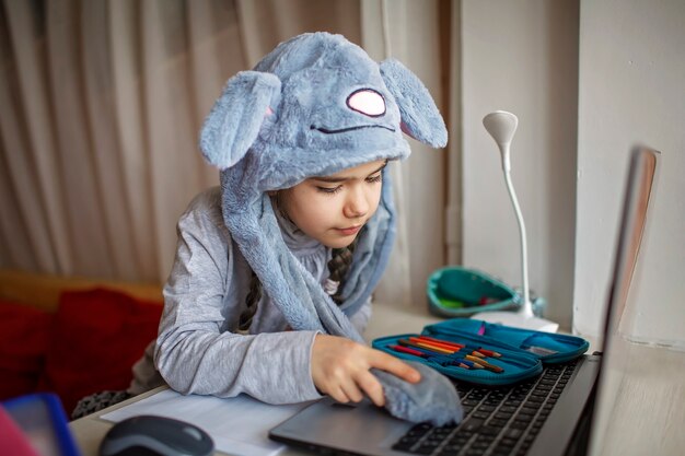 Pretty schoolgirl wearing funny rabbit hat with ears during boring online lesson