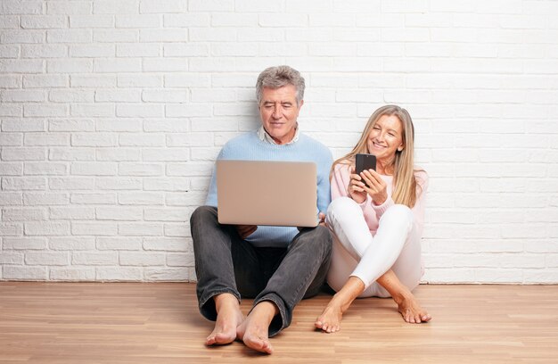 Pretty senior couple sitting on their house floor with a laptop