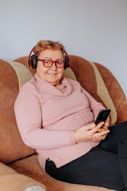 自宅のソファに座ってヘッドフォンでお気に入りの音楽を楽しんでいるかなり年配の女性