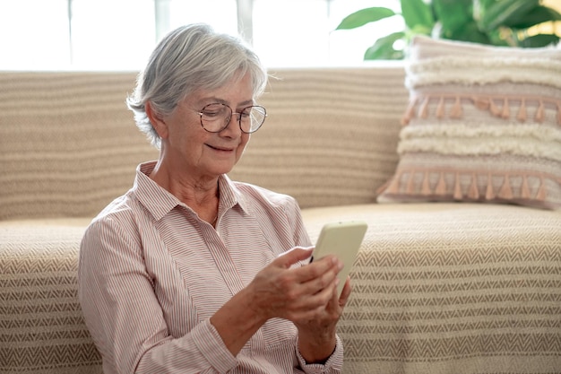 Довольно пожилая женщина расслабилась, сидя на полу, держа смартфон в руках Улыбающаяся зрелая дама