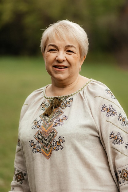 Pretty senior woman in traditional ukrainian embroidered shirt on park background