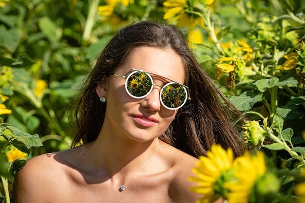 Pretty sensual young brunette in sunglasses in a field of blooming sunflowers young woman portrait