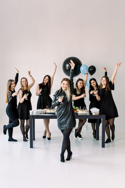 Фото Довольно семь красивых стильных женщин в элегантном повседневном черном наряде празднуют новый год, день рождения, веселятся, танцуют, пьют алкогольные коктейли