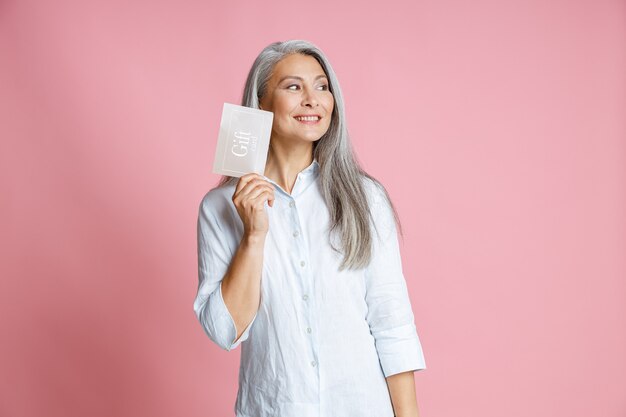 Pretty silver haired Asian woman holds gift card having ideas in studio