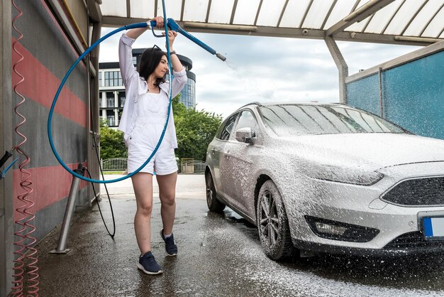 Una ragazza piuttosto magra lava la sua auto con la schiuma della pistola. concetto di pulizia