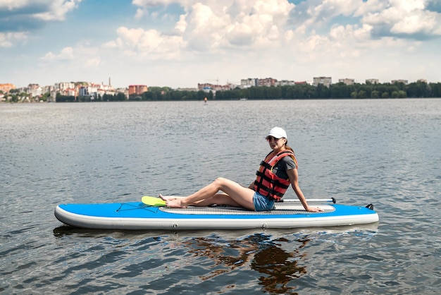 Pretty slim woman floats on sup board and long paddle on city lake