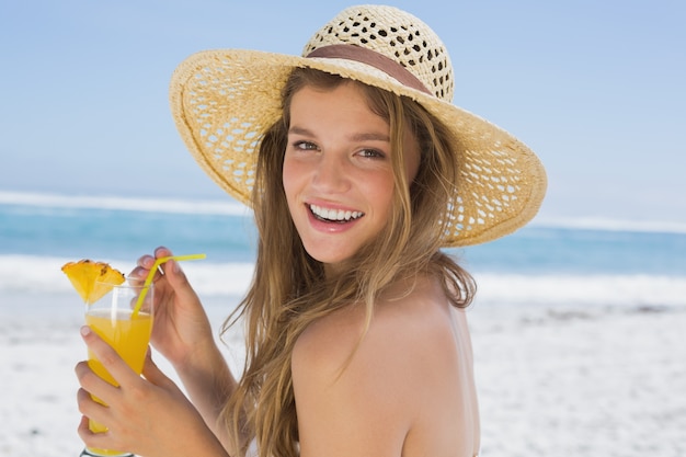 Pretty smiling blonde in bikini holding cocktail on the beach