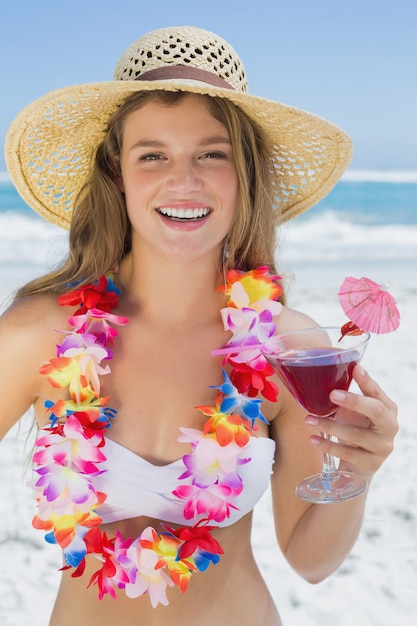 Pretty smiling blonde in floral garland holding cocktail on the beach