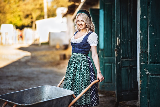 Pretty smiling blonde in traditional dress with wheelbarrow working in backyard.