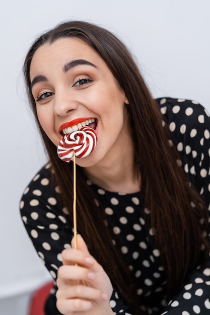 Photo pretty smiling brunette girl with a lollipop in her hand. candy on stick.