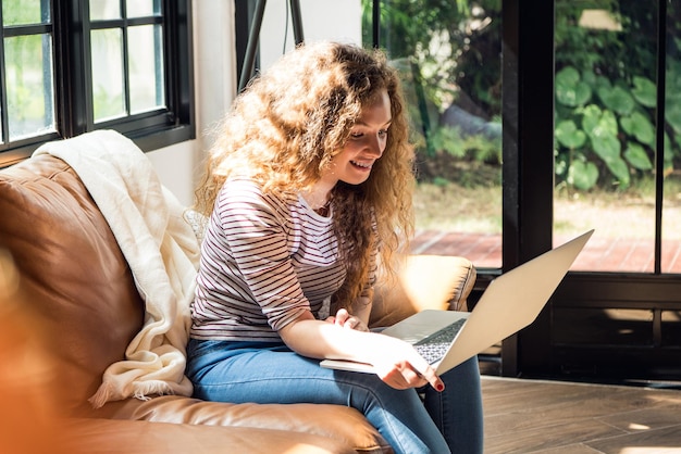 Pretty smiling Caucasian woman using laptop computer on the couch at home