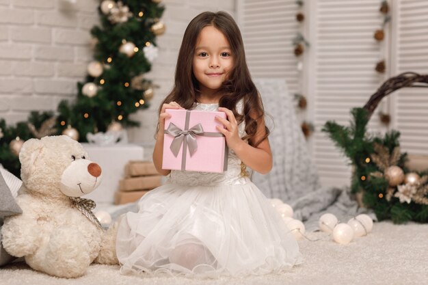 Ragazza sorridente graziosa che tiene il regalo di natale in mano a casa