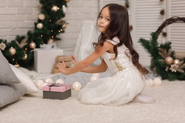 Pretty smiling girl holding Christmas gift in hand at home