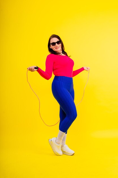 Pretty smiling plump female in sporty top and leggings holding jumping rope in hands