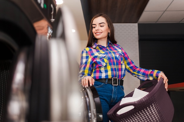 Pretty smiling woman at the laundromat holds a basket of clothes.