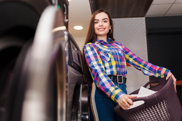 Pretty smiling woman at the laundromat holds a basket of clothes.