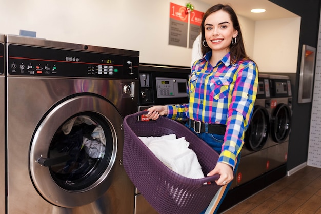 Pretty smiling woman at the laundromat holds a basket of clothes.