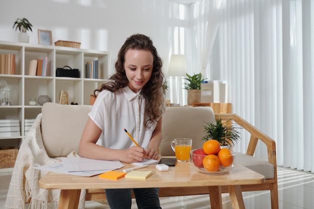 Pretty smiling young businesswoman working on project at home due to lockdown